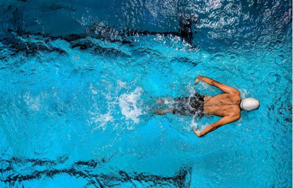 man in zwembroek met badmuts aan het zwemmen in een zwembad